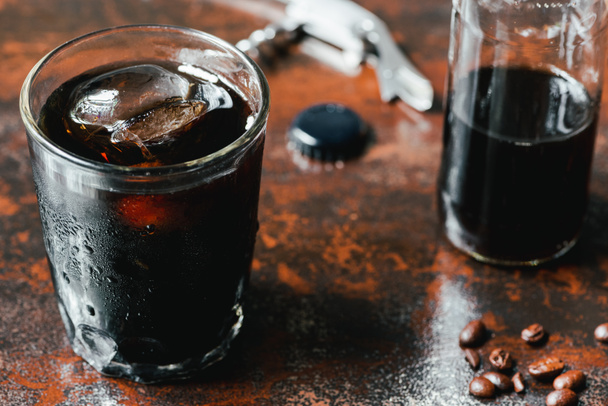 selektivní zaměření studené kávy s ledem ve skle a láhvi v blízkosti kávových zrn na rezavém povrchu - Fotografie, Obrázek