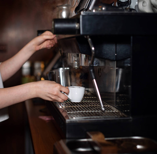 Meisje maakt espresso in een koffiezetapparaat. Barista is koffie aan het zetten. Koffieshop, restaurant, horecagelegenheid. Close-up handen maken een drankje - Foto, afbeelding