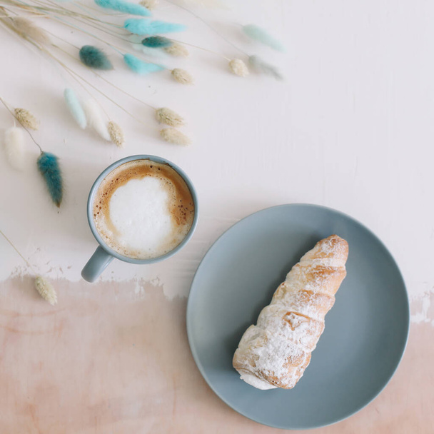 Frühstück mit Bäckerei und Kaffee. Blätterteigrollen mit Sahne auf einem Teller und Cappuccino. Ansicht von oben - Foto, Bild