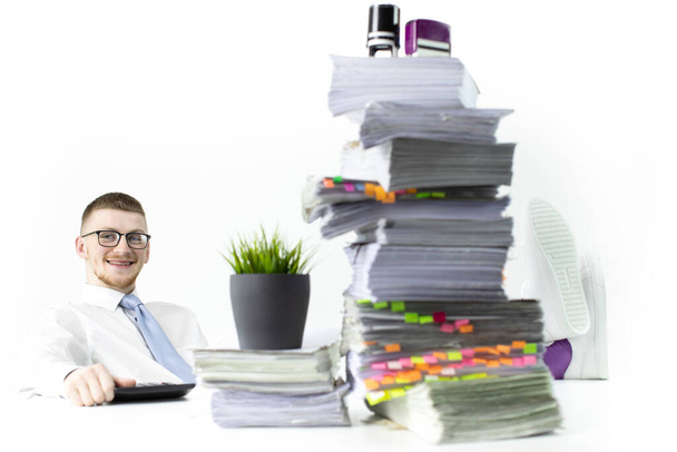 Feliz oficinista se sienta con las piernas sobre una mesa llena de papeles y sellos
 - Foto, Imagen