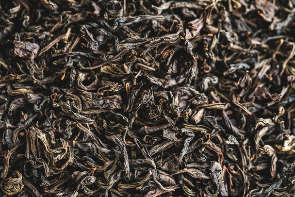 Fekete nagy levelű tea, mint háttér. Száraz fekete tealevelek szerkezete. Sötét háttér. Makró üzemmód. fekete levél tea közelről - Fotó, kép