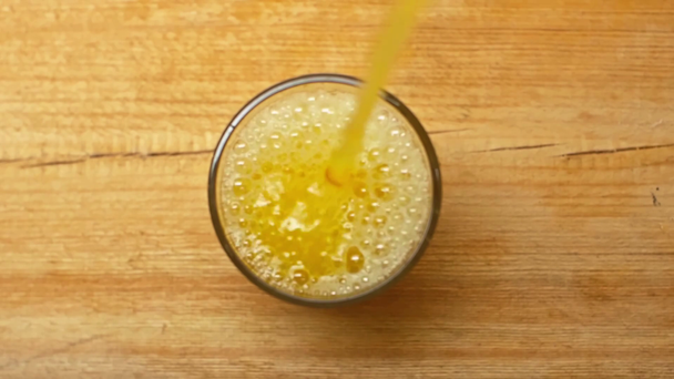 Hidas liike appelsiinimehua kaatamalla lasiin puupinnalla - Materiaali, video