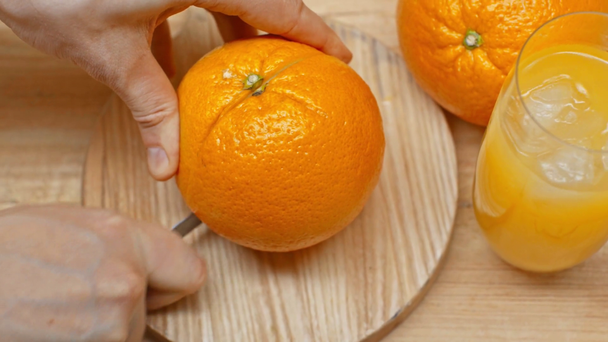 Ausgeschnittene Ansicht eines Mannes, der Orangen in der Nähe eines Saftglases auf einer Holzoberfläche schneidet - Filmmaterial, Video