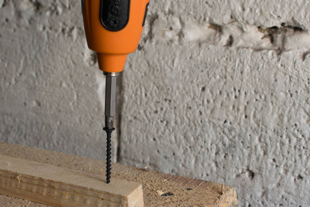 Een man schroeft een zelftappende schroef in een houten vloer met een elektrische schroevendraaier. - Foto, afbeelding