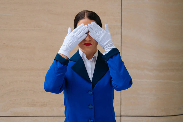 A flight attendant in a blue suit with white gloves covered her face with her palm. The concept of fear in flight. . High quality photo - Foto, imagen