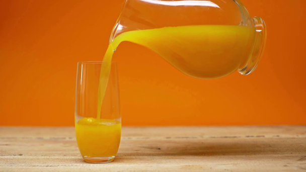 Man pouring orange juice in glass on wooden surface isolated on orange - Video