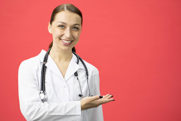 Jovem bonita sorridente médico aponta para espaço de texto vazio no fundo vermelho
 - Foto, Imagem