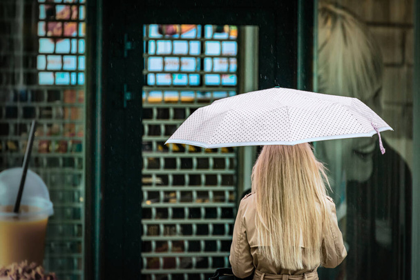Ein Mädchen unter einem Regenschirm steht an einem regnerischen Tag vor einem geschlossenen Geschäft. - Foto, Bild