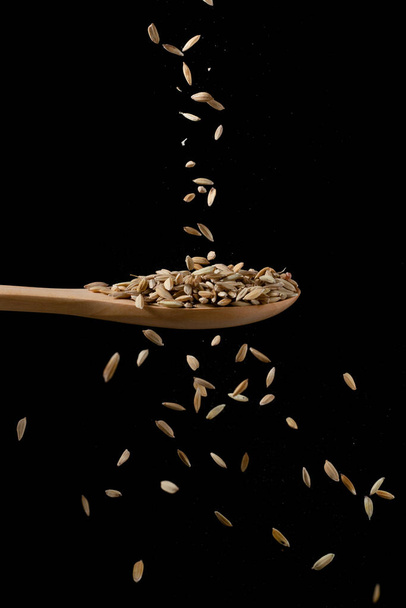 Reis auf einen Kochlöffel streuen. Fließender Reis auf schwarzem Hintergrund. - Foto, Bild