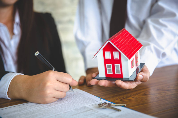 Zakenmensen en klanten ondertekenen overeenkomsten voor de aankoop van huizen. Hand houden van de pen ondertekening koopcontract. Grijze daken en sleutels dicht bij elkaar geplaatst.. - Foto, afbeelding