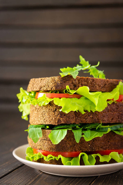 Sandwiches con lechuga y rúcula, tomate y pepino, sándwiches veganos de pan negro grueso con verduras frescas
 - Foto, imagen