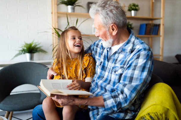 Happy little girl with cute grandfather reading story book at home - Photo, image