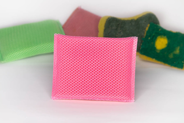 Nueva esponja para lavar platos La esponja es de color rosa y tiene una malla que cubre la esponja. Y tiene una vieja esponja característica a través del uso colocado detrás y fondo blanco
 - Foto, Imagen