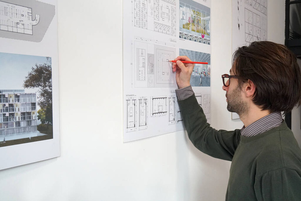 Jovem arquiteto homem com notas de desgaste casual em seu plano de construção - Foto, Imagem