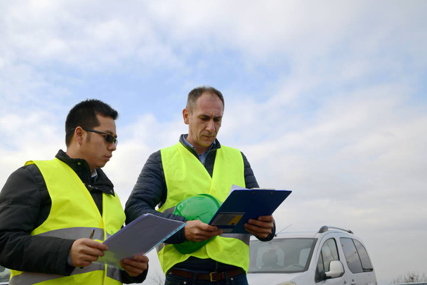 Інженер, який показує щось на папері своєму начальнику на нещодавно побудованому шосе
 - Фото, зображення
