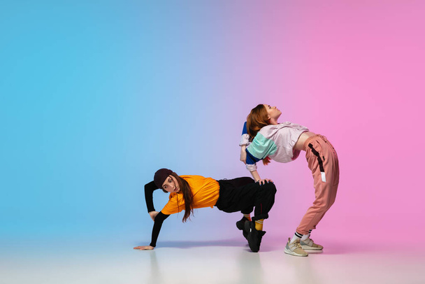 Girls dancing hip-hop in stylish clothes on gradient background at dance hall in neon light. - Photo, Image