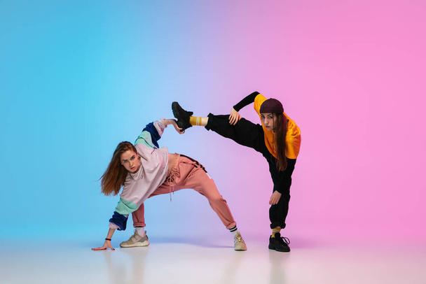 Girls dancing hip-hop in stylish clothes on gradient background at dance hall in neon light. - Fotografie, Obrázek