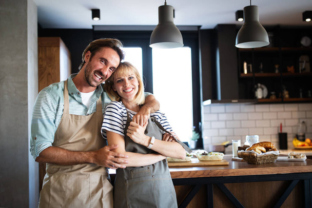 Beautiful young lovely couple is talking and smiling while cooking healthy food in kitchen at home - Photo, Image