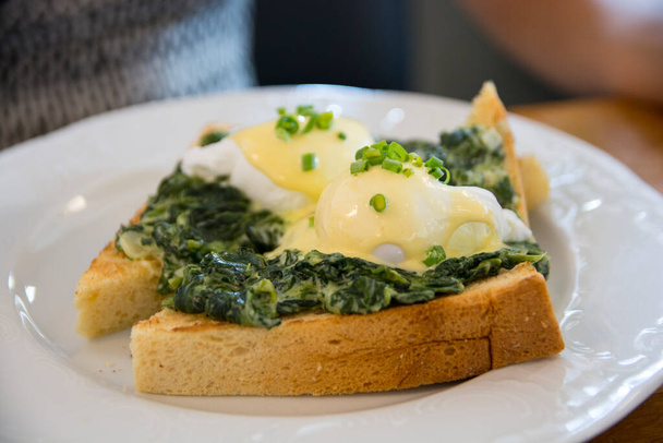 Παραδοσιακά αυγά Benedict Florentine με αυγά ποσέ. σπανάκι με κρέμα, πράσινα κρεμμύδια, σάλτσα Hollandaise και μοσχοκάρυδο, πάνω από ένα ψωμί - Φωτογραφία, εικόνα