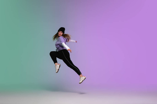 Κορίτσι που χορεύει χιπ-χοπ σε κομψά ρούχα με κλίση φόντο στην αίθουσα χορού σε νέον φως. - Φωτογραφία, εικόνα
