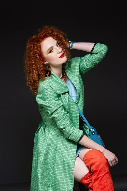 girl with red hair and white skin, curly curly hair, lush hairstyle, red lipstick, beautiful makeup, green polto and orange long boots - Foto, Bild