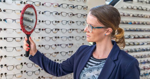 ビジネスの女性は光学店で鏡の前で眼鏡をかけて - 写真・画像