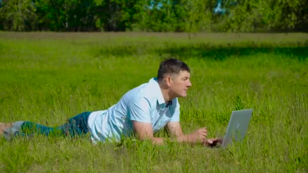 İşadamı çimlerin üzerinde duran bir dizüstü bilgisayarın arkasında çalışıyor. - Video, Çekim