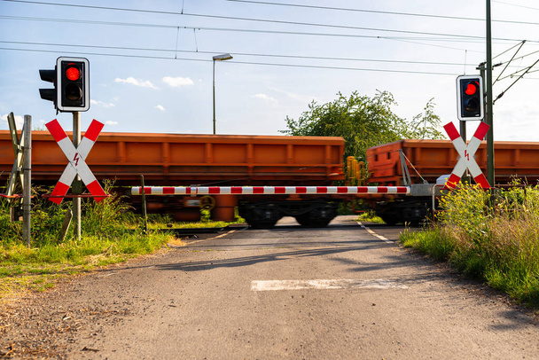 Closed barrier at the railroad crossing with red warning lights on, visible blurred red wagons in motion.  - Φωτογραφία, εικόνα