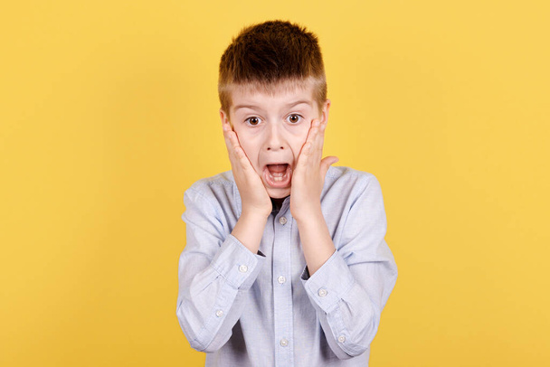 Portrait of a brunette boy scared. Isolated on yellow background. - Фото, изображение