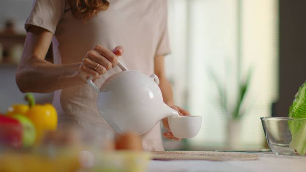 Женщина наливает чай в чашку на кухне. Женщина пьет чай дома
 - Фото, изображение