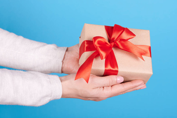 Present box with red ribbon in hands on blue background. - Fotografie, Obrázek