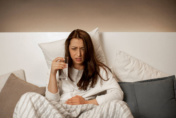 blank meisje in bed met kussens ervaringen acute pijn als gevolg van menstruatie - Foto, afbeelding