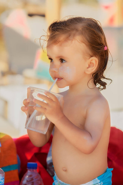 Bebek, kumsalda pipetle su içiyor. - Fotoğraf, Görsel