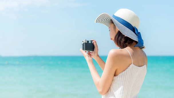 Životní styl mladá žena relaxovat na letní pláži. Asie turisté drží fotoaparát a fotit na pláži na dovolené, modrá obloha pozadí. Koncept letních prázdnin.  - Fotografie, Obrázek