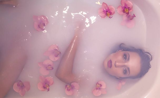 όμορφη κοπέλα που ποζάρει σε ένα μπάνιο γεμάτο γάλα και λουλούδια για φωτογραφίες - Φωτογραφία, εικόνα