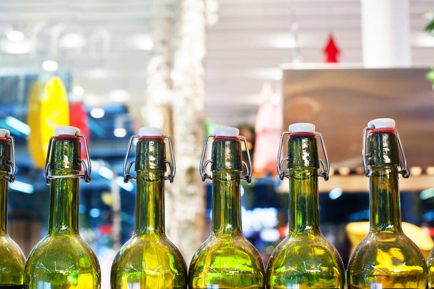 Πράσινα γυάλινα μπουκάλια κρασιού στη σειρά σε ξύλινο ράφι, μπαρ εσωτερικό σχεδιασμό, την προετοιμασία των αλκοολούχων κοκτέιλ, κρασί γεύση έννοια, στυλ νυχτερινή ζωή, παραγωγή οινοποιείο, θολή φόντο από κοντά - Φωτογραφία, εικόνα