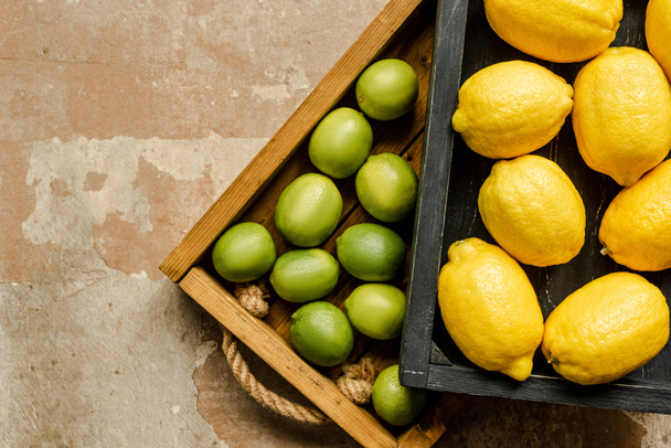 top view of lemons and limes in wooden boxes on weathered surface - Foto, Imagem