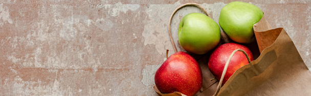 πάνω όψη χάρτινης τσάντας με κόκκινα και πράσινα μήλα σε φθαρμένη μπεζ επιφάνεια, πανοραμική καλλιέργεια - Φωτογραφία, εικόνα