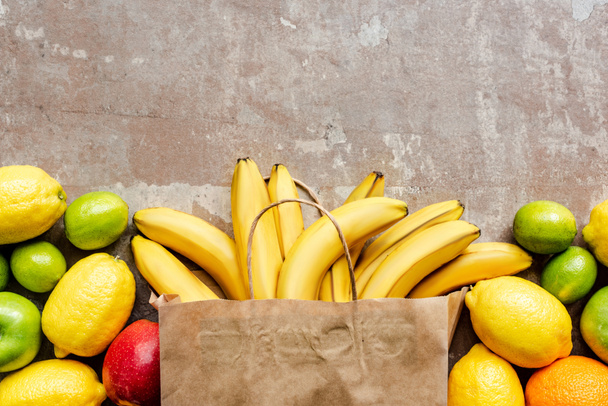 top view of paper bag with colorful fresh fruits on beige weathered surface - 写真・画像