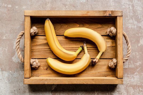 top view of ripe bananas in wooden box on weathered surface - Foto, imagen