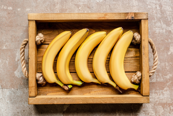 top view of ripe bananas in wooden box on weathered surface - Foto, imagen