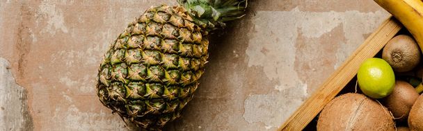 top view of ripe pineapple near wooden box with fruits on weathered surface, panoramic crop - Valokuva, kuva