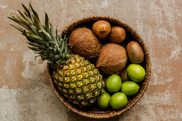 top view of ripe exotic fruits in wicker basket on weathered surface - Foto, immagini