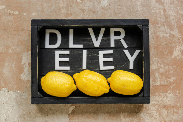 vista superior de entrega de palabras cerca de limones en caja negra de madera en superficie erosionada
 - Foto, imagen
