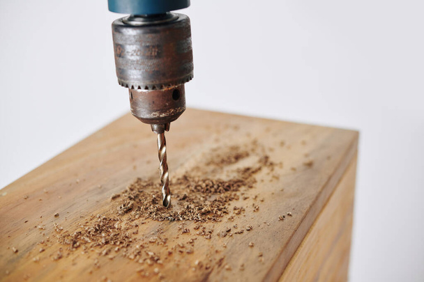 Imagen de cerca de taladro eléctrico haciendo agujero en tablón de madera al hacer muebles en taller - Foto, imagen