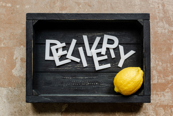 vista superior de entrega de palabras cerca de limón en caja negra de madera en superficie erosionada
 - Foto, Imagen
