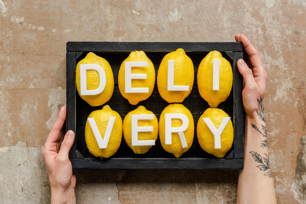 partial view of woman holding wooden box with word delivery on lemons on weathered surface - Photo, Image