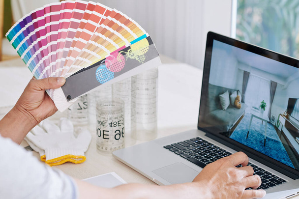 Designer d'intérieur regardant des photos inspirantes sur l'écran d'ordinateur portable et choisissant la couleur pour la couleur des murs de la palette - Photo, image