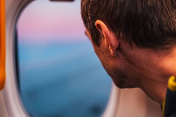 άνθρωπος κοιτάζοντας μέσα από φινιστρίνι του αεροπλάνου σε μπλε φόντο του ουρανού  - Φωτογραφία, εικόνα