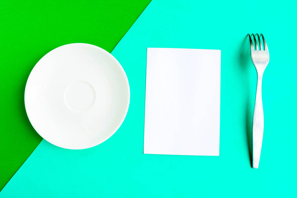 White mockup plate, fork and paper blank on green background. Copy space for the text. Minimal concept - Photo, Image
